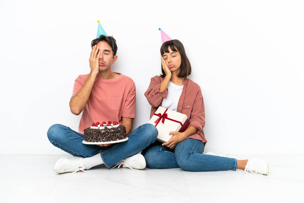 Nuori sekoitettu rotu pari juhlii syntymäpäivää istuu lattialla eristetty valkoisella taustalla yllätys ja järkyttynyt kasvojen ilme - Valokuva, kuva