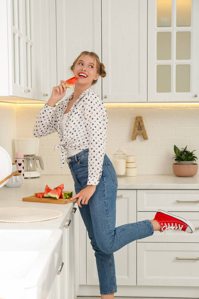 Beautiful teenage girl with slice of watermelon near countertop in kitchen - Фото, зображення