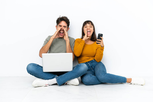 Молода пара з ноутбуком і мобільним, сидячи на підлозі кричачи і оголошуючи щось
 - Фото, зображення