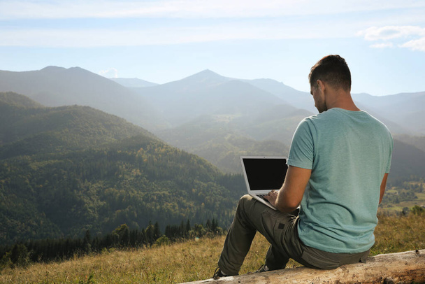 Man working with laptop in mountains on sunny day - Zdjęcie, obraz