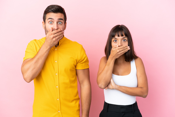 Young couple isolated on pink background covering mouth with hands for saying something inappropriate - 写真・画像