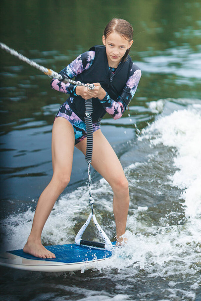 Active beautiful girl in the swimsuit standing on the wakeboard in the river - Photo, Image