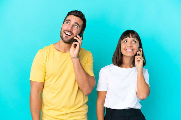 Молодая пара изолированы на синем фоне ведения разговора с кем-то мобильный телефон - Фото, изображение