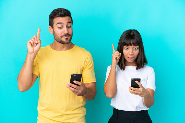 Молода пара ізольована на синьому фоні за допомогою мобільного телефону та підйомного пальця
 - Фото, зображення