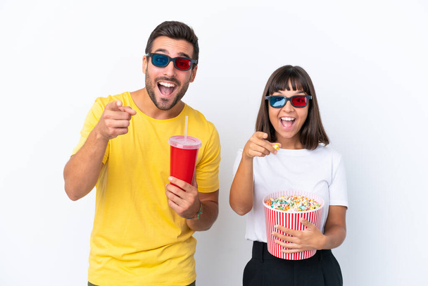 Junges Paar isoliert auf weißem Hintergrund mit 3D-Brille und hält einen großen Eimer Popcorn, während es nach vorne zeigt - Foto, Bild
