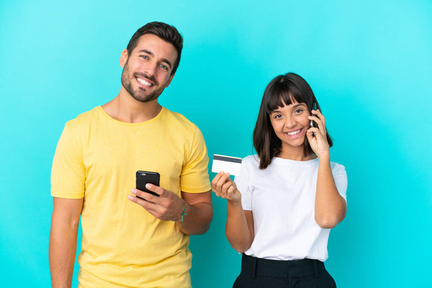 Fiatal pár elszigetelt kék háttér miközben egy beszélgetést a mobiltelefon és a kezében egy hitelkártya - Fotó, kép