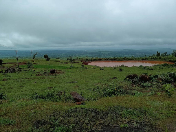 Scenic view of small pond full of brown color water in the middle of the farmland or agricultural filed, picture captured during monsoon season at sateri hills , Kolhapur, Maharashtra, India. - Photo, Image