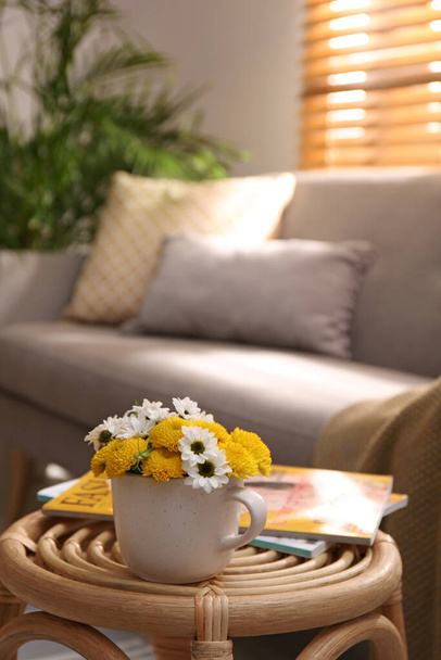 Cup with beautiful bright flowers and magazines on table in living room, space for text - Fotografie, Obrázek
