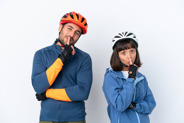 白い背景に隔離された若いサイクリストのカップルは、口を閉じて沈黙のジェスチャーの兆候を示しています - 写真・画像