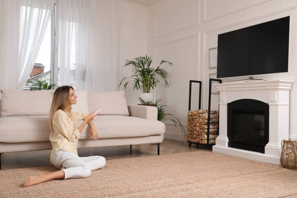 Young woman watching television at home. Living room interior with TV on fireplace - Фото, изображение