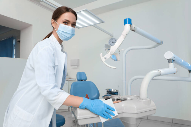 Professional dentist in white coat and medical mask cleaning workplace indoors - Fotografie, Obrázek