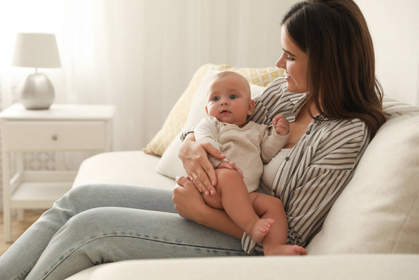 Young woman with her little baby on sofa at home - Foto, imagen