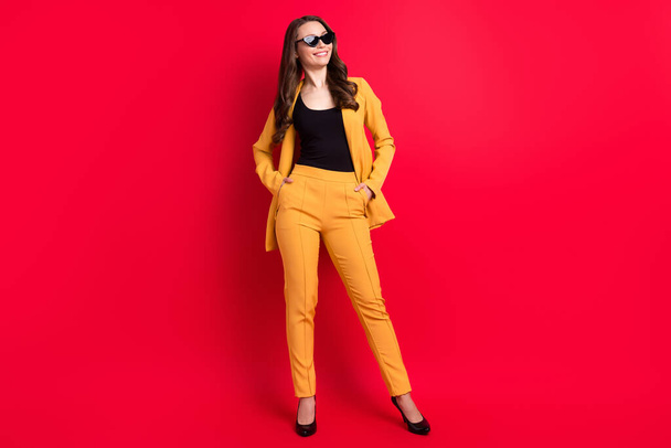Photo of charming funny lady dressed yellow blazer dark glasses smiling arms pockets empty space isolated red color background - Fotografie, Obrázek