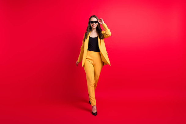 Full length body size view of attractive cheerful cool girl going touching specs isolated over bright red color background - Фото, изображение