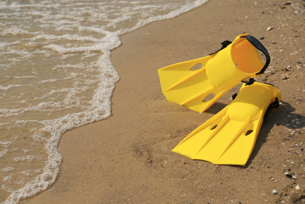 Pair of yellow flippers on sand near sea. Space for text - Φωτογραφία, εικόνα