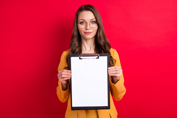 Photo of pretty charming young lady dressed yellow blazer glasses smiling holding clipboard empty space isolated red color background - Photo, Image