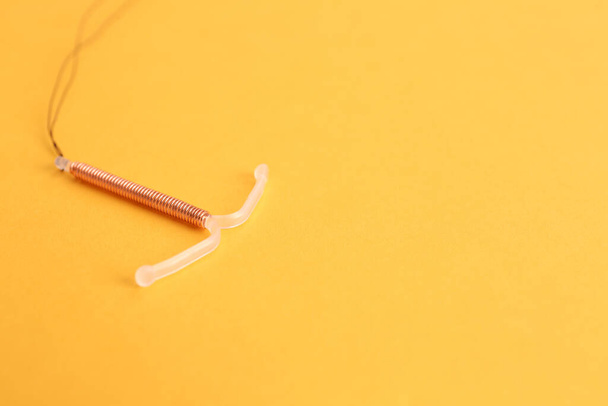 Copper intrauterine contraceptive device on yellow background. Space for text - 写真・画像
