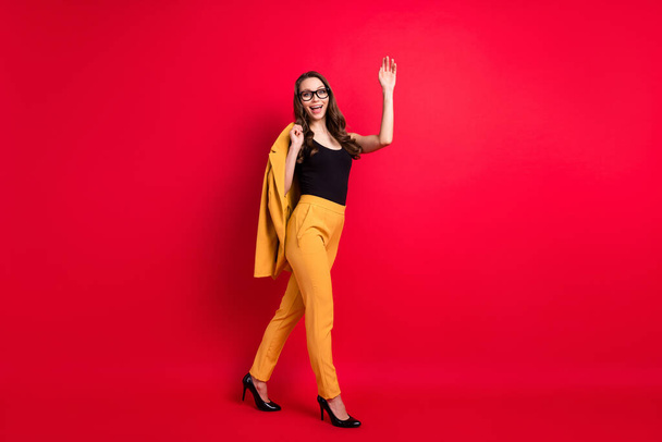 Full length body size view of attractive chic slim fashionable cheerful lady walking waving hi hello isolated on shine red color background - Fotó, kép