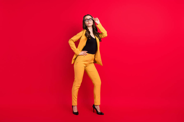 Photo of confident cool young lady dressed yellow blazer glasses arm waist looking empty space isolated red color background - 写真・画像
