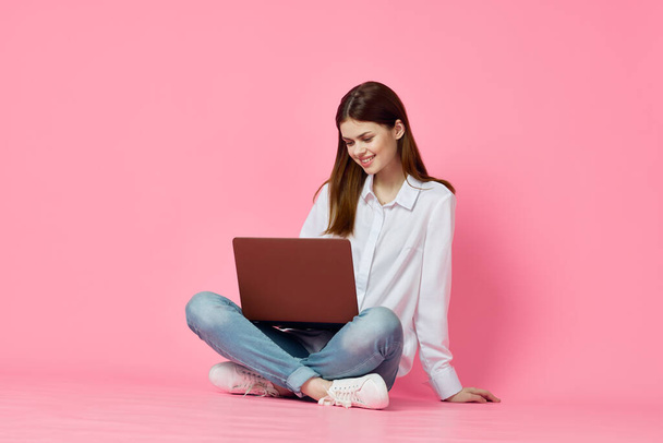 mujer sentada en el suelo con ordenador portátil en línea compras tecnología rosa fondo - Foto, Imagen
