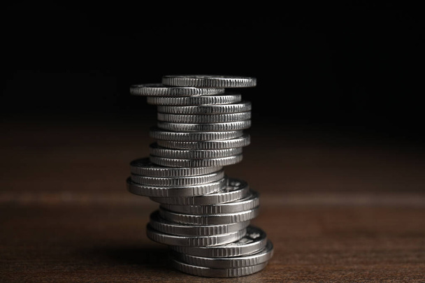 Many coins stacked on wooden table against black background - Photo, Image