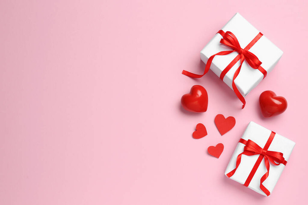 Beautiful gift boxes and red decorative hearts on pink background, flat lay. Space for text - 写真・画像
