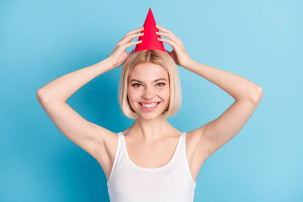 Photo of satisfied girl toothy smile arms touch red hat look camera isolated on blue color background - Φωτογραφία, εικόνα