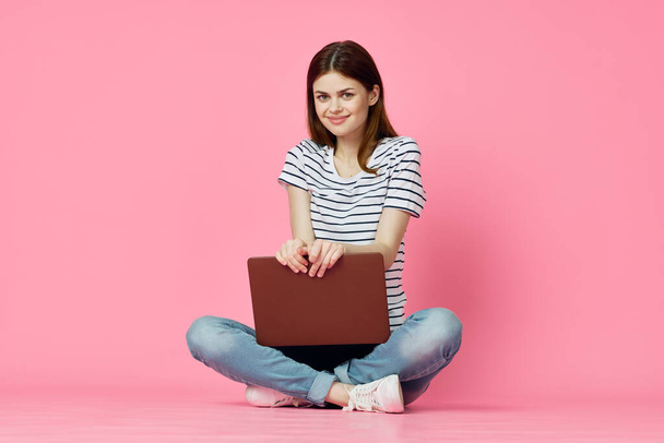 cheerful woman with laptop sitting on the floor on a pink background - Foto, Imagen