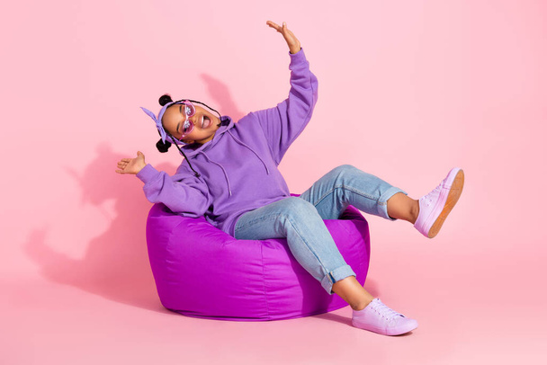 Photo of funny funky afro woman wear purple hoodie buns sitting beanbag fooling smiling isolated pink color background - Фото, изображение