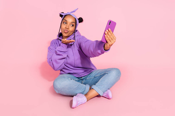 Photo of beautiful attractive afro woman wear purple hoodie buns sending arm kiss modern device isolated pink color background - Фото, изображение