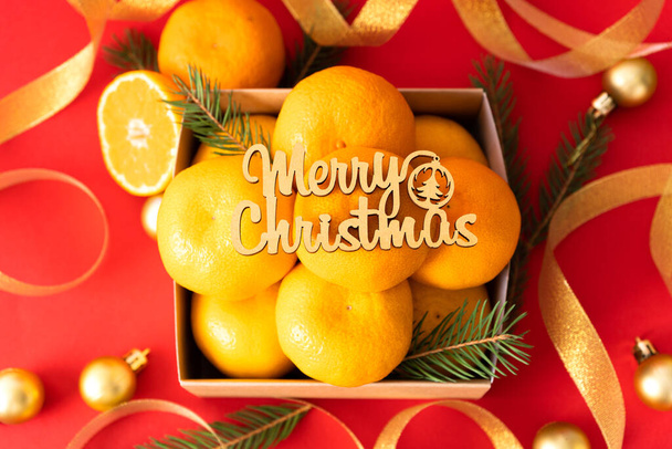 Tangerinky v papírové krabici jsou zdobeny vánočními ozdobami a stuhami s borovými větvemi. - Fotografie, Obrázek
