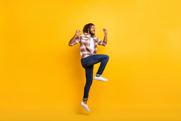 Foto de cuerpo de longitud completa del hombre saltando alto gesto como ganador de la lotería riendo aislado en el fondo de color amarillo vibrante - Foto, imagen