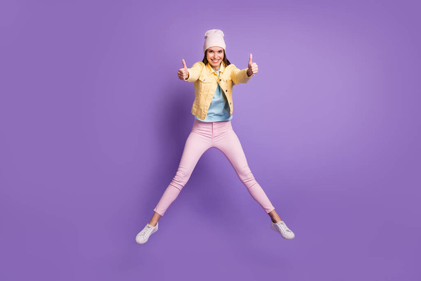 Full length body size photo of young woman jumping showing like thumb-up sign both hands isolated on vibrant purple color background - 写真・画像