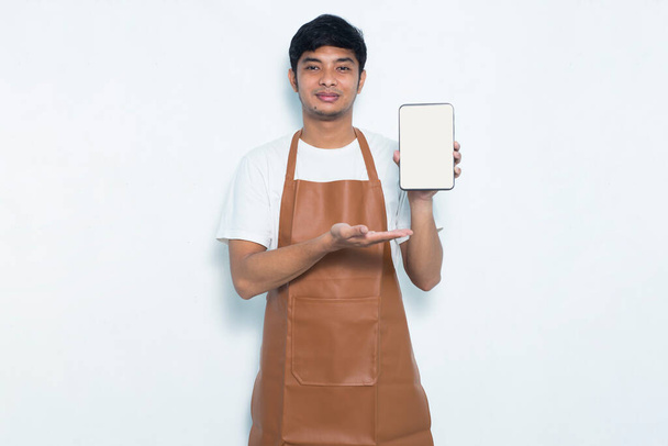 Счастливый молодой азиатский мужчина бармен или официантка демонстрирует мобильный телефон на белом фоне - Фото, изображение