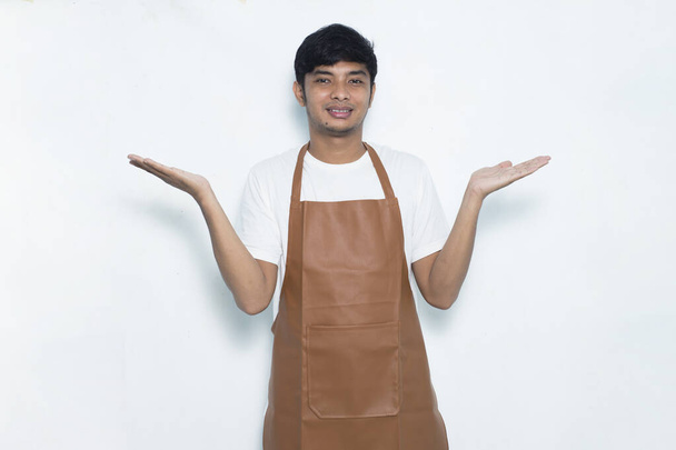 Щасливий молодий азіатський чоловік бариста офіціантка вказує пальцями в різні боки ізольовані на білому тлі
 - Фото, зображення