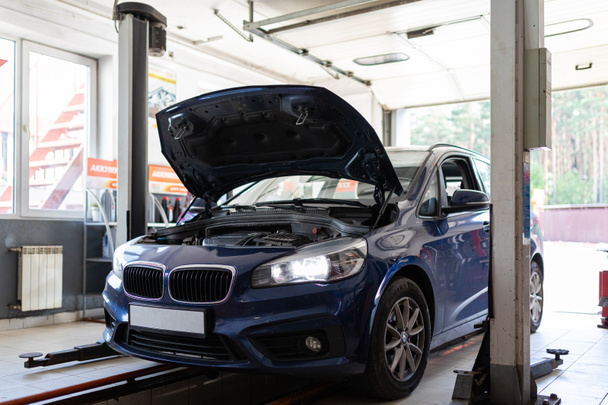 Benzin istasyonundaki mavi bir yolcu aracının açık bir kaputla tamir edilirken fotoğrafı. - Fotoğraf, Görsel