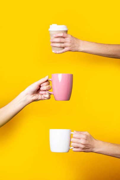 Три руки держат чашки и бумажный стакан на желтом фоне - Фото, изображение