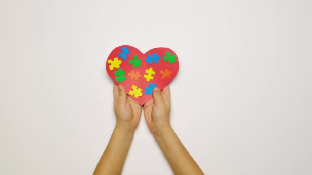 Çocuk, anne ve baba avuçlarında otizmin sembolü olan renkli yapboz parçaları taşıyan bir kalp taşıyor. Otizm spektrum bozukluğu olan ailelere destek. Dünya Otizm Farkındalık Günü. Akrabaların sevgisi - Video, Çekim