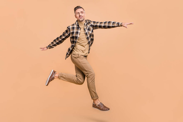 Full size profile side photo of mature man carefree arms wings playful run jump isolated over beige color background - Fotó, kép
