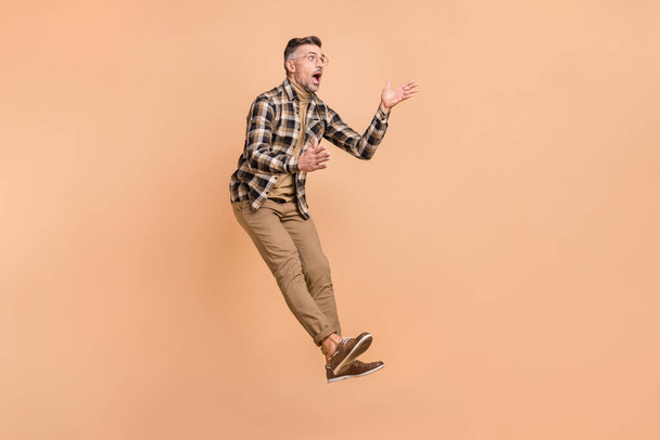 Full body profile side photo of astonished mature man jumper reaction look empty space isolated over beige color background - Foto, Bild