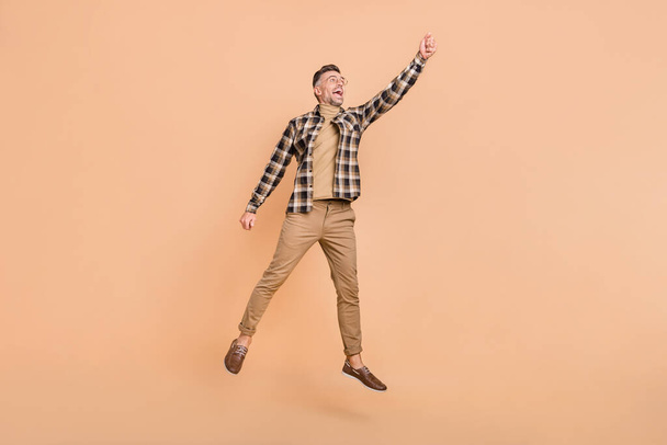Full size photo of mature man jump up try to catch umbrella look empty space isolated over beige color background - Fotografie, Obrázek