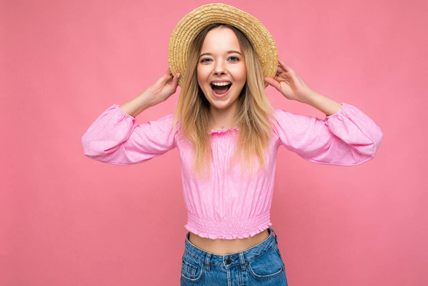 Photo shot młodej pięknej blondynki ładny szczęśliwy noszenie stylowy różowy blat i słomkowy kapelusz izolowane na różowym tle z miejsca kopiowania - Zdjęcie, obraz