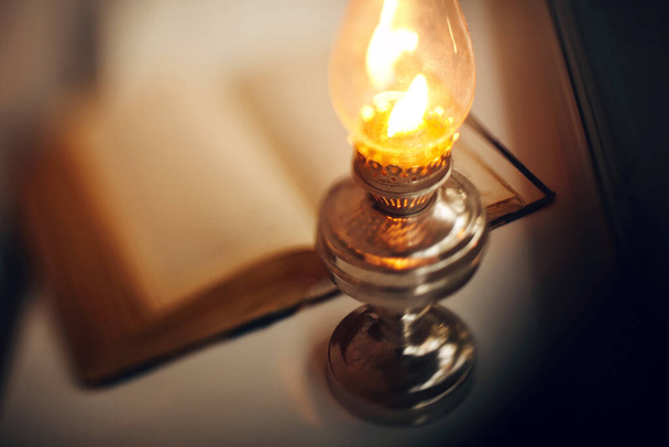 Vintage kerosene lamp burning and old open book - Foto, afbeelding