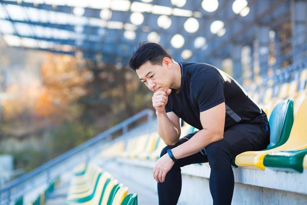 Frustrated Asian male athlete depressed, dissatisfied with the result of his training, in despair after running, resting sitting - Valokuva, kuva