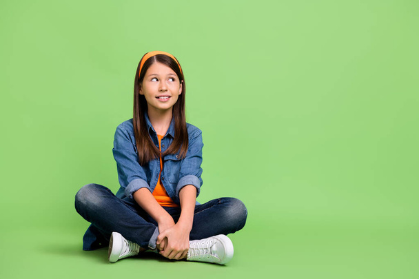 Full size photo of nice little girl sit look promo wear shirt jeans hairband footwear isolated on green background - Фото, зображення