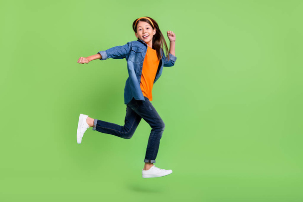 Photo of funky sweet preteen girl dressed jeans shirt running fast jumping high smiling isolated green color background - Valokuva, kuva