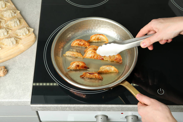 Woman cooking gyoza on frying pan with hot oil in kitchen, closeup - Φωτογραφία, εικόνα