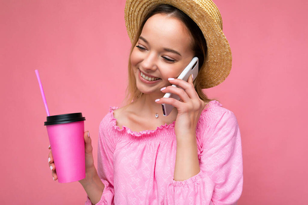 Szczęśliwa młoda kobieta rozmawia przez telefon komórkowy, pijąc kawę na różowym tle - Zdjęcie, obraz