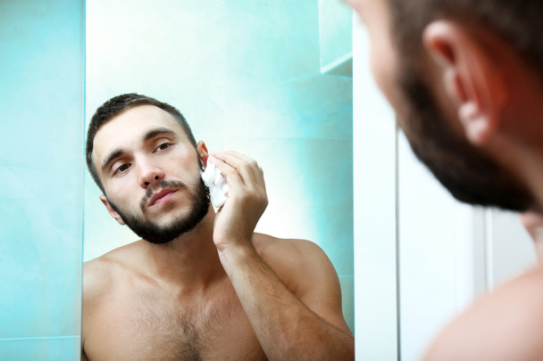 Young man shaving his beard in bathroom - Fotoğraf, Görsel
