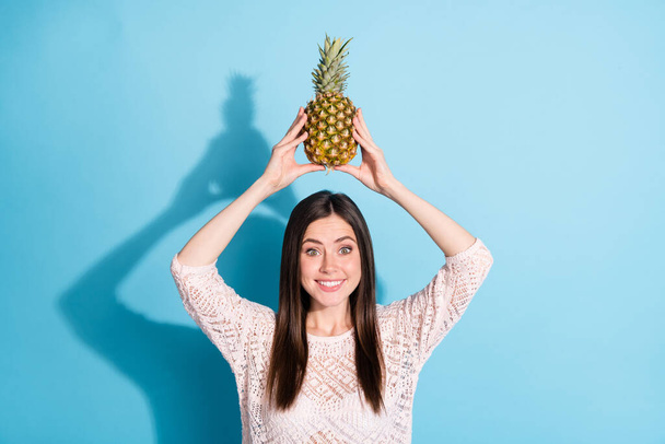 Photo of amazed excited happy young woman hold pineapple above head isolated on blue color background - Fotoğraf, Görsel
